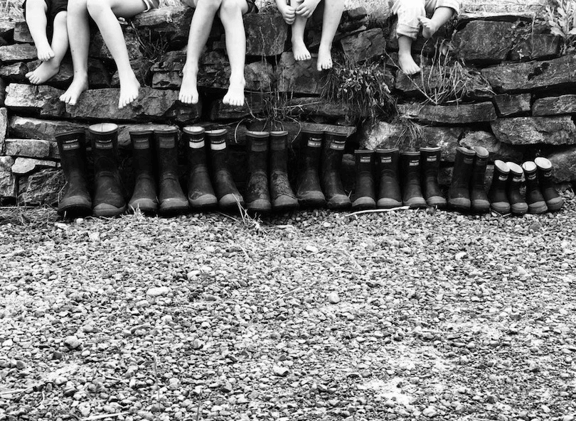 Black and white photo of eight pairs of Red Bands lined up against a wall. Above each pair, you can see a child sitting, legs dangling. 