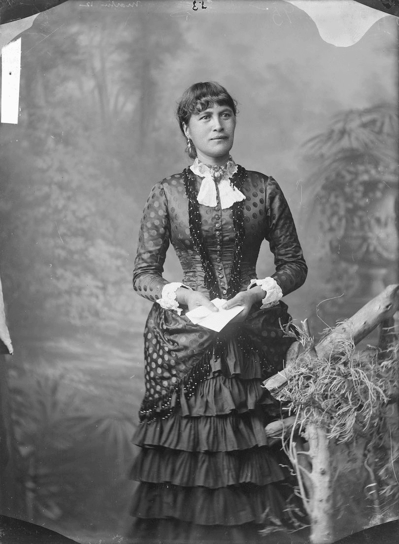 Black and white photograph of a young Māori woman wearing a beautiful corseted dress.