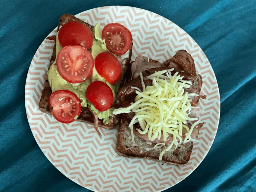 A photo of two epic pieces of toast: one covered in avo and tomatoes, the other in bacon topped with a massive handful of grated cheese.