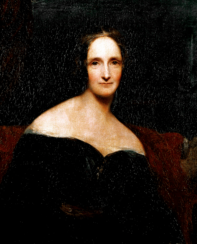 Portrait of a woman – emphasis is on her glowing skin and strong gaze; she wears a black off the shoulder gown, hair pulled back and no jewellery. 