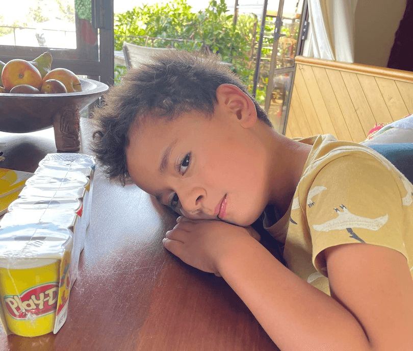 Photo of a young boy with his head resting on a table, looking knackered but contented, a line-up of PlayDo tubs on the table.