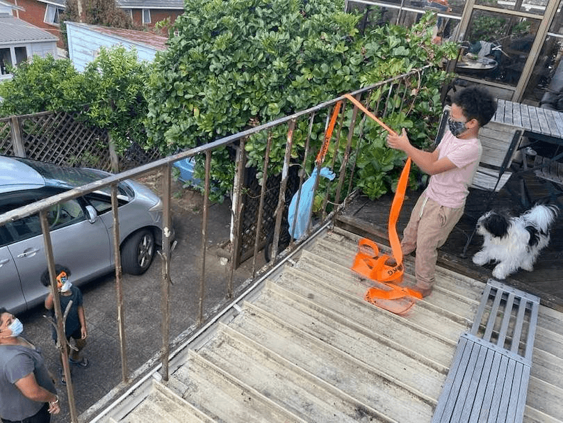 Photo taken from a balcony where a young boy is delightedly pulling up a bag of treats. Two adults watch from below, beaming.