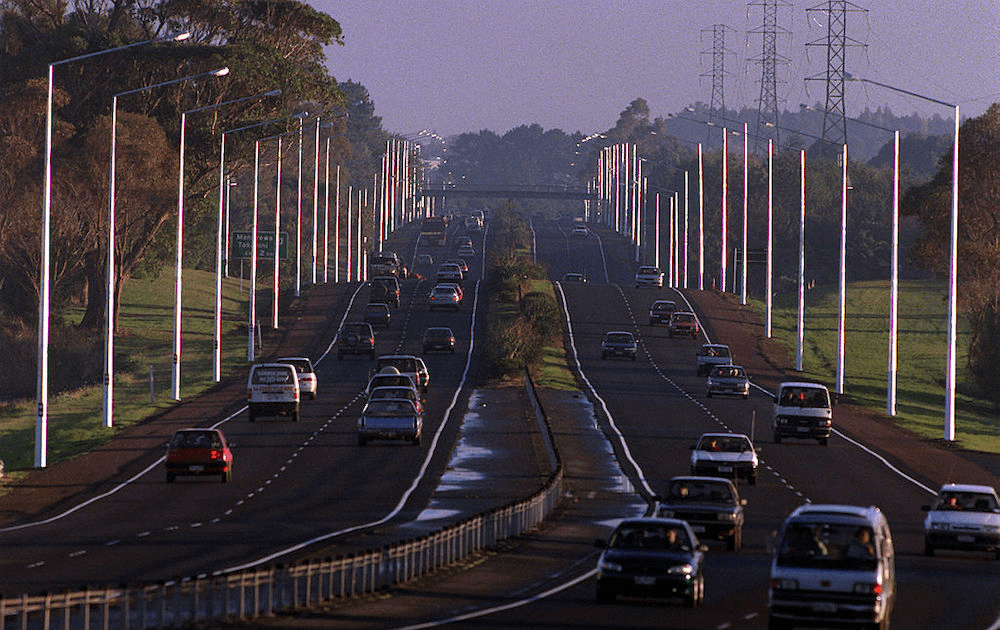 a purple morning with rows and rows of cars progressing in a straight line down a auckland motorway
