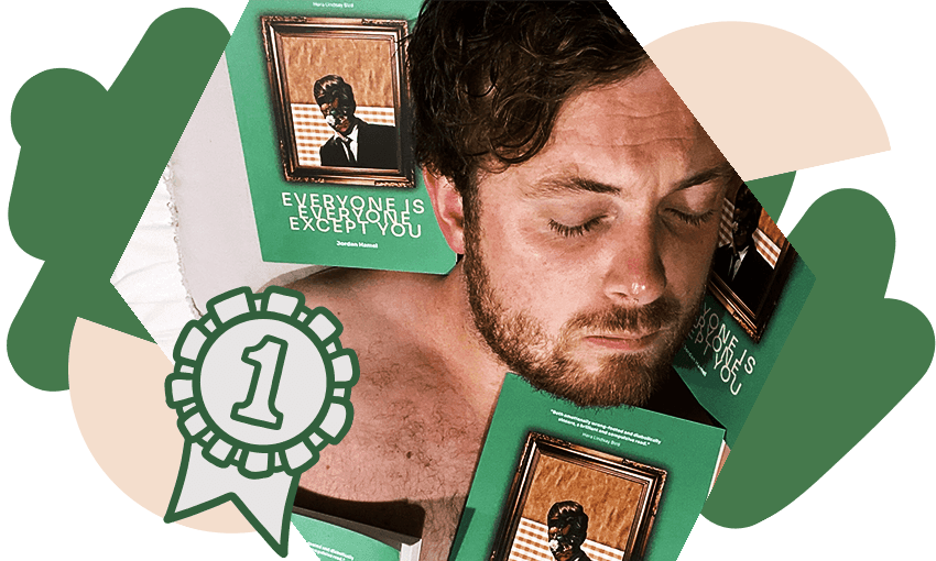 Photo of a young, bearded man, sleeping topless nestled into copies of his book of poetry.