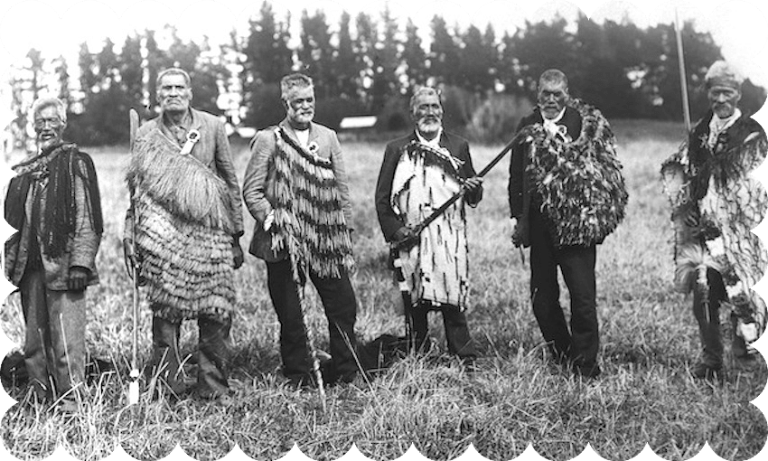 Black and white photograph of six Māori men standing in a row, facing the camera. All wearing various styles of kākahu over their suits.