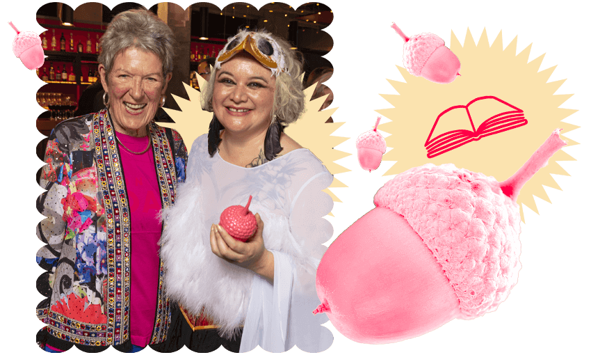 Photograph of two very happy women, one holding a trophy in the shape of a pink acorn. Other pink acorns are zooming around as design elements, with book emojis.