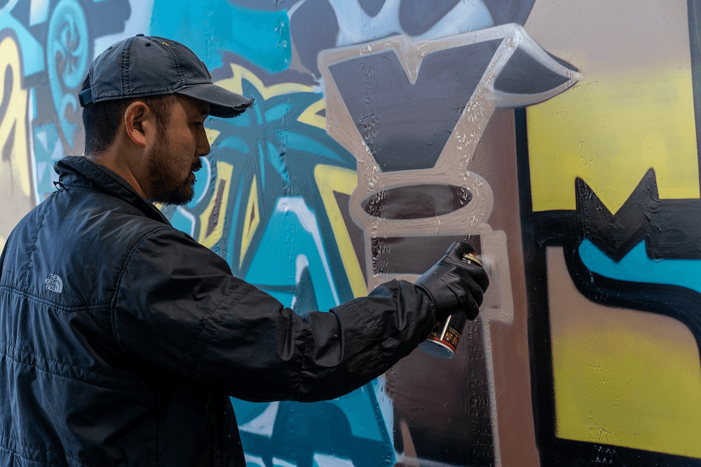 Bobby Hung, wearing a black cap and jacket, ads the finishing touches to a blue and yellow mural