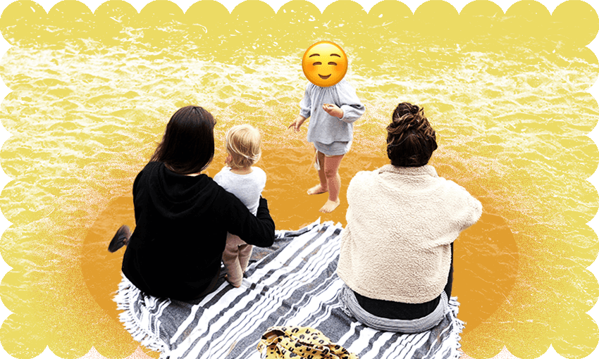 a family has a picnic on the beach. one child is shown with only the back of their head visible; one child has a smiling emoji over their face