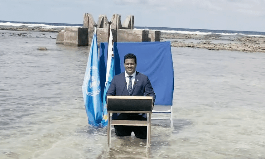 a man in a suit standing in clear tropical seas at a lectern delivering a UN address