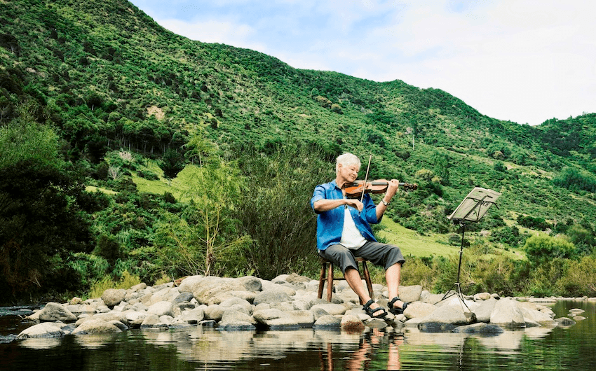 Jeanette Fitzsimons plays violin on the Kauaeranga river (Photo: Bev Short) 
