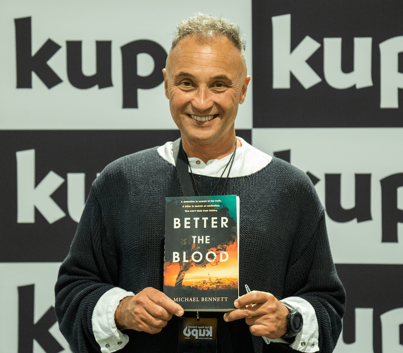 Photograph of a smiling Maori man holding a copy of his book Better the Blood. 