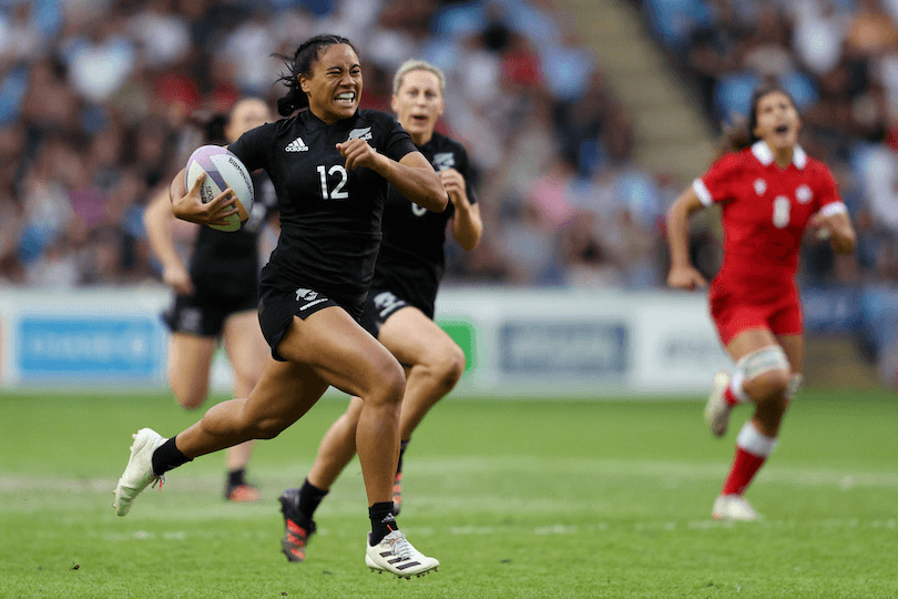Photo of a woman grimacing as she races with ball in hand, other players in her wake.