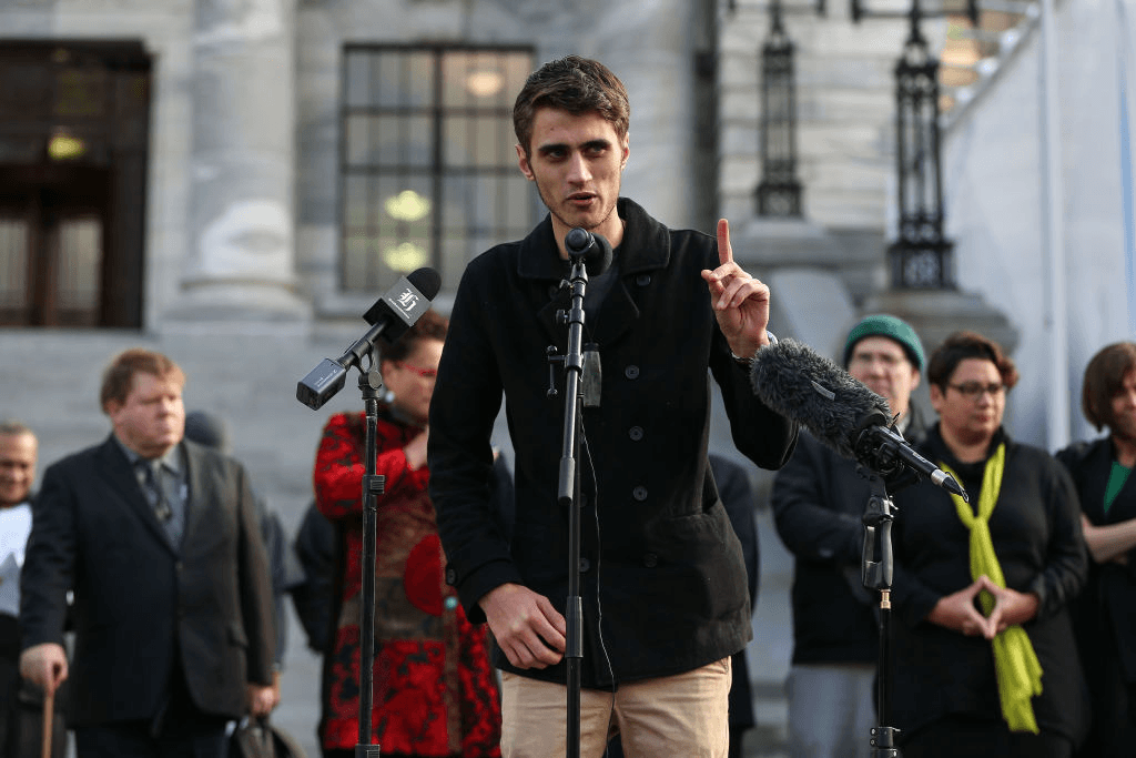 Tupua Urlich speaking at a microphone in front of the New Zealand parliament building