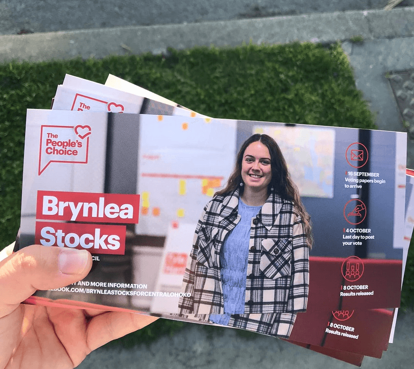 hand holding pamphlet of stocks, young white presenting woman in black and white coat