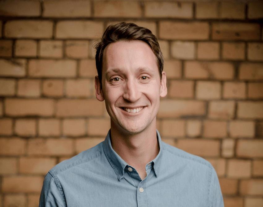 dave cameron, a youngish white man, smiles in front of a brick wall