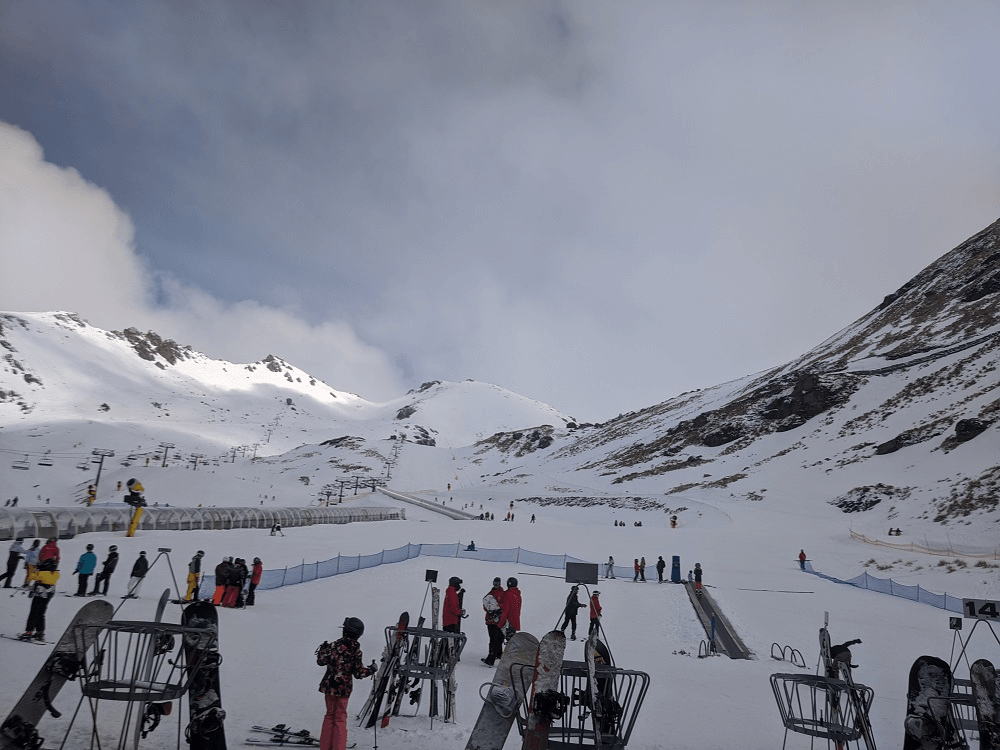 lots of skiiers and snowboarders clusterd in foreground with mountain and lifts in background