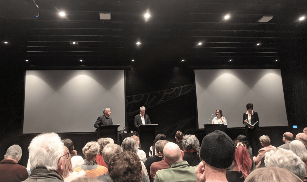 stage with 4 people - 2 chrichstchurch 2022 mayoral candidates and two white women who are asking questions. lots of mostly grey heads visible in the audience