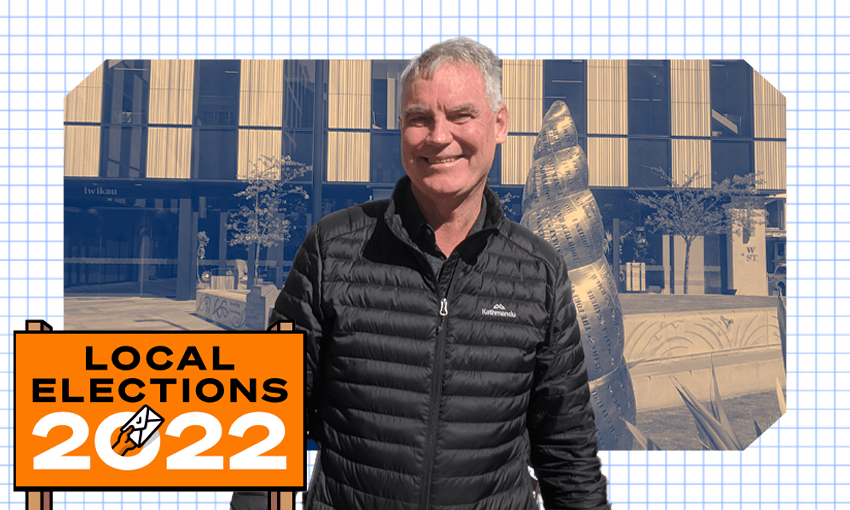david meates, a white man in a puffer vest, smiles in the sunshine with a sculpture in the background and a local elections 2022 sign in front of him