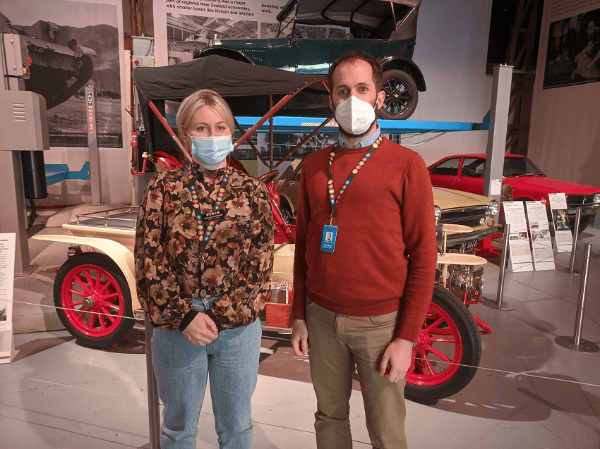 a white man and woman wearing masks in front of a vintage car