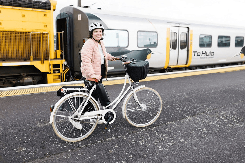 louise huttt a brunette white woman with a bike and a pink jacket stands in front of a train