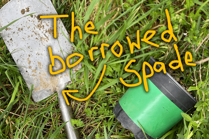 The borrowed spade lying in the grass next to a potted plant