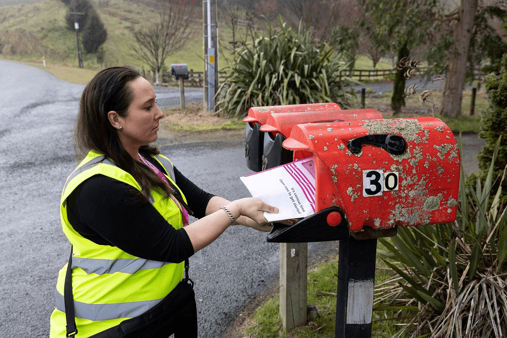 womanin hi vis jacket putting a purple census form in a red lichen covered letterbox, it looks like a rainy day! 