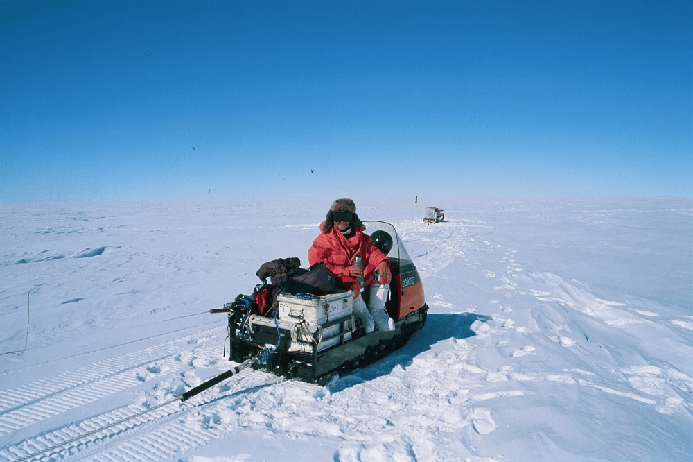 endlessly blue sky and that impossible gleaming horizon. in the centre of the frame, a scientist in a red coat cups a mug in his hands. it is very sunny, very empty, very cold
