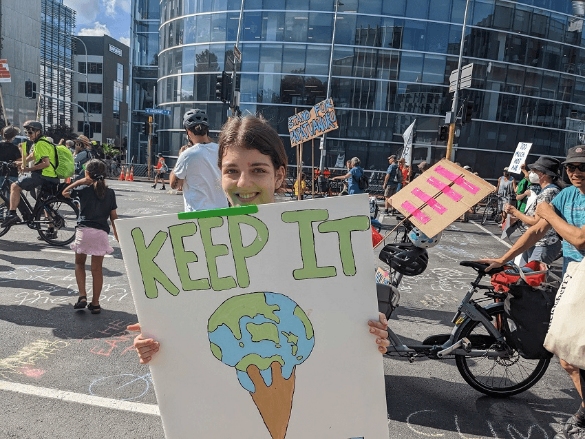 lots of signs in the background, sunny day , person with brown hair in a small bun and a sign saying 'keep it cool' with the earth as a melting icecream. it is not shanti's best ever photographic work