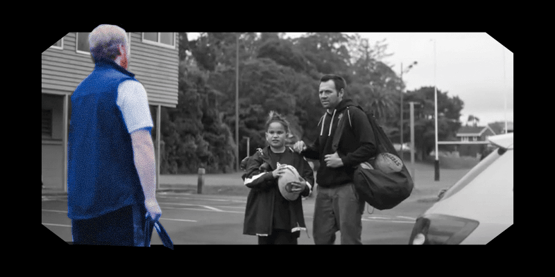 A frame from the Corrections ad, showing a Pākehā corrections officer facing a Māori man and his son. The officer is in colour while the rest of the image is black and white