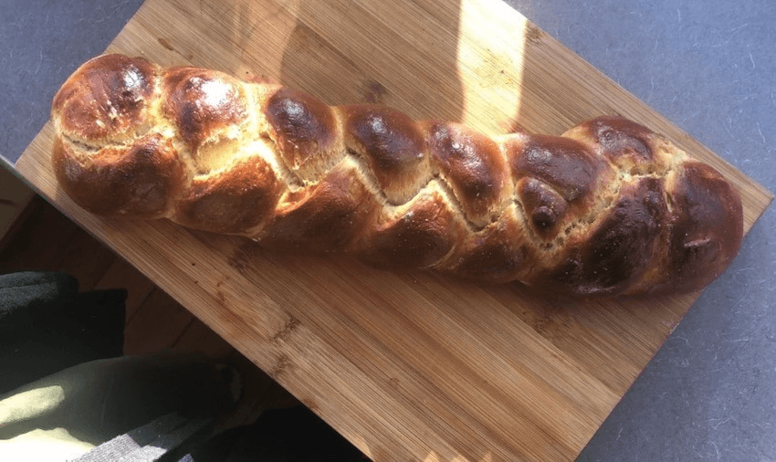 A loaf of braided challah bread on a wooden board. The photograph is taken from a bird's eye view.