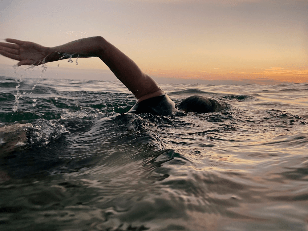 sunset and still water, a person's arm pushing them through the sea