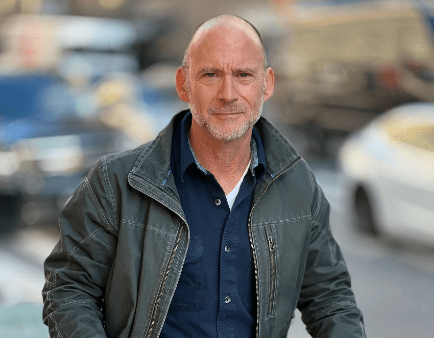 bald white man with out of focus city in background, and a very cool green leather jacket 