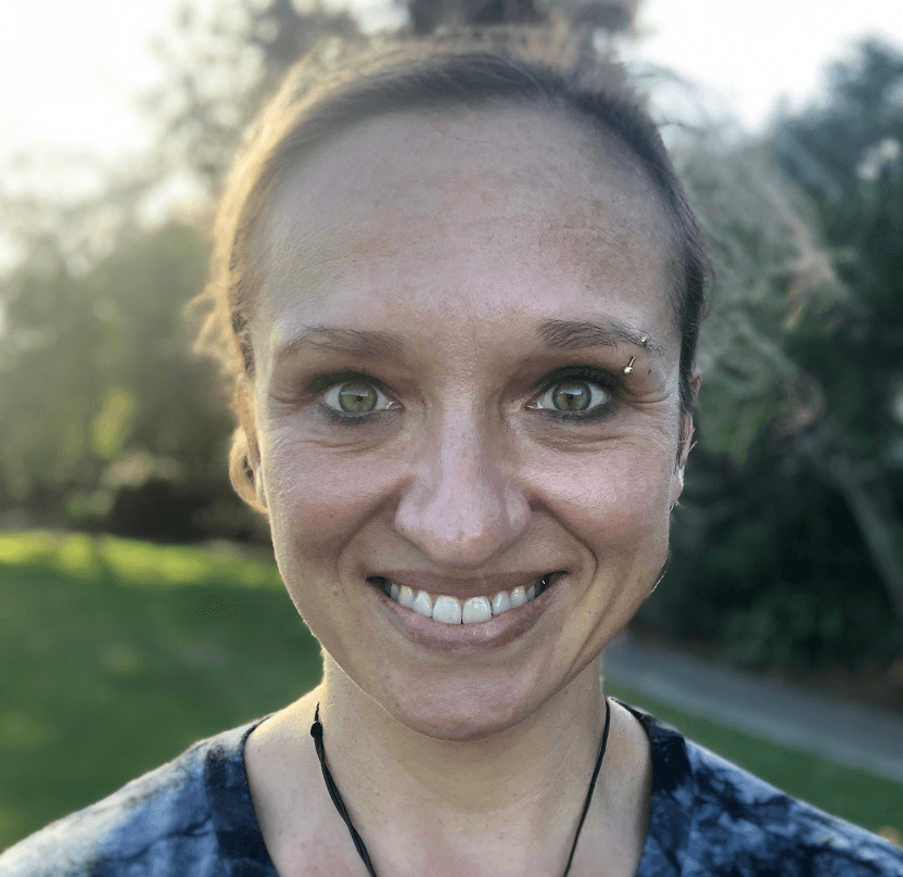 woman with a big smile and an eyebrow piercing and green behind her