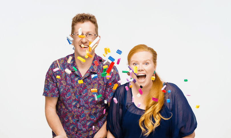 A man and woman throw colourful Lego blocks into the air and laugh