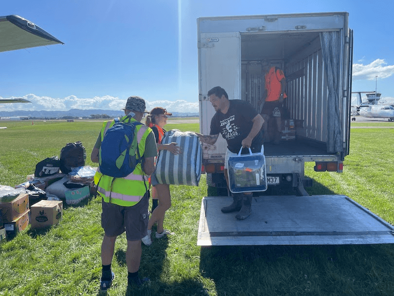 people handing out supplies from a truck against a green field backdrop