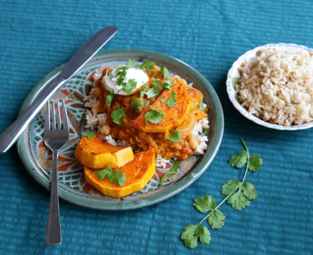 Pumpkin and lentil curry. Served with rice on a mosaic design plate on a blue tablecloth.