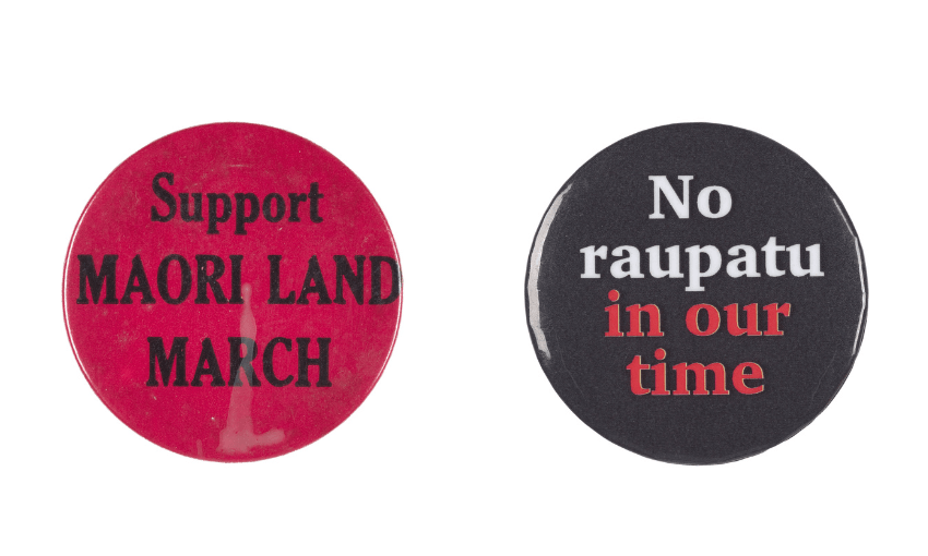 A photograph of two badges side by side. One saying Support Maori Land March and the other saying No raupatu in our time
