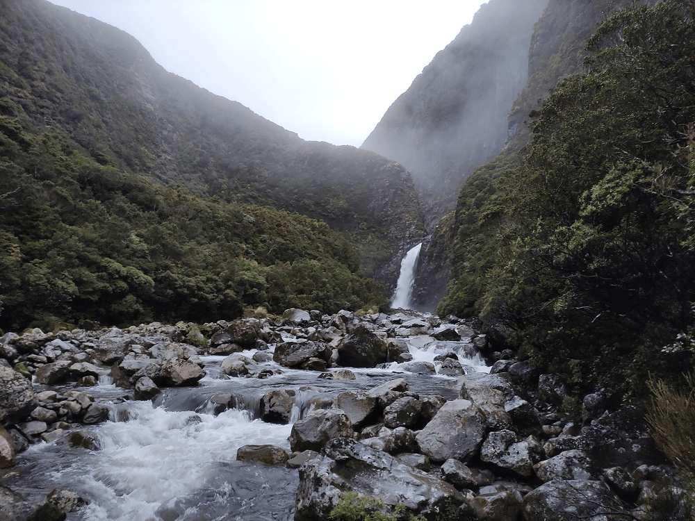 misty mountains and a stream with slippery rocks and steep bushy hills rising into the sky