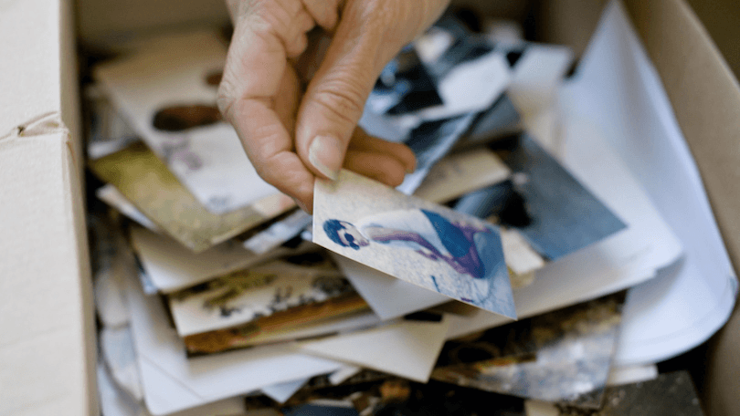 a hand holds a photo of a young man, with a pile of photos in the background