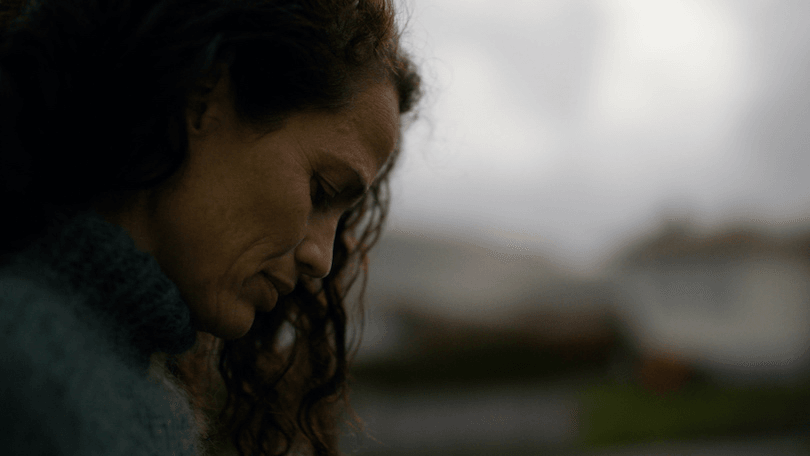 A close-up side-on view of a woman with long hair, looking down