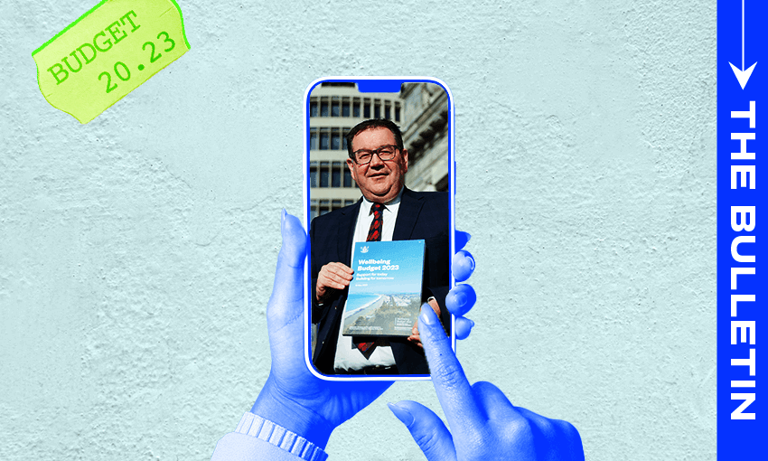 A person scrolls on a phone that has a picture of Grant Robertson holding a copy of this year's Budget