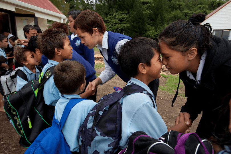 a group of Māori children hongi each other outside their school