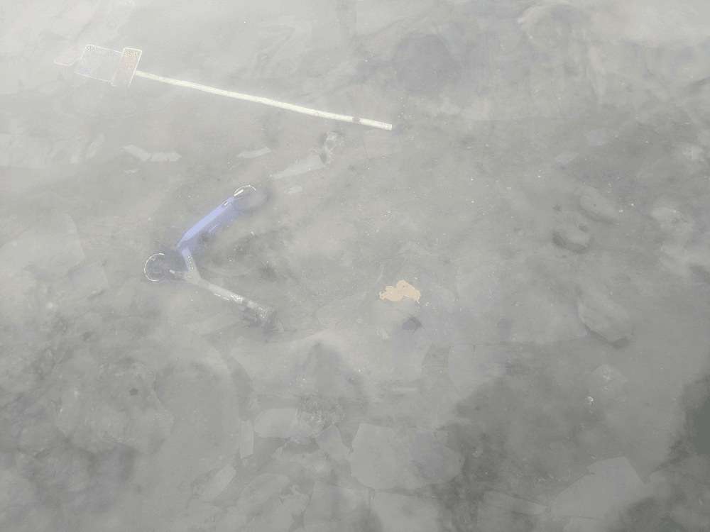 grey glassy water surface and a sad looking purple Beam escooter lying askew underwater