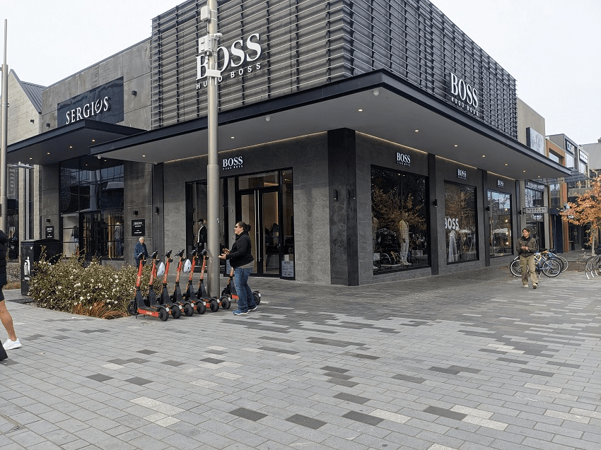 the grey mosaic of tiles with a black office/retail building behind and some very neatly parked orange neon Neron scooters