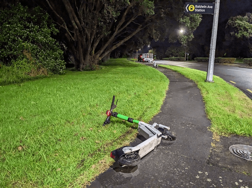 it's nightime and a lime e-scooter lies, fetchingly on its side, blocking part of the footpath
