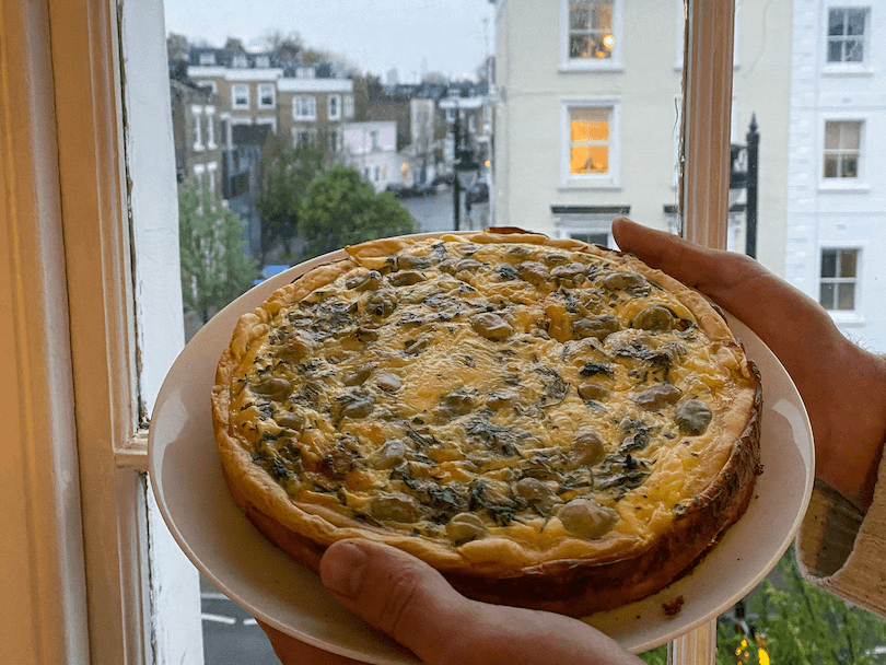 a quiche on a plate held up against a window out of which you can see a London street scene