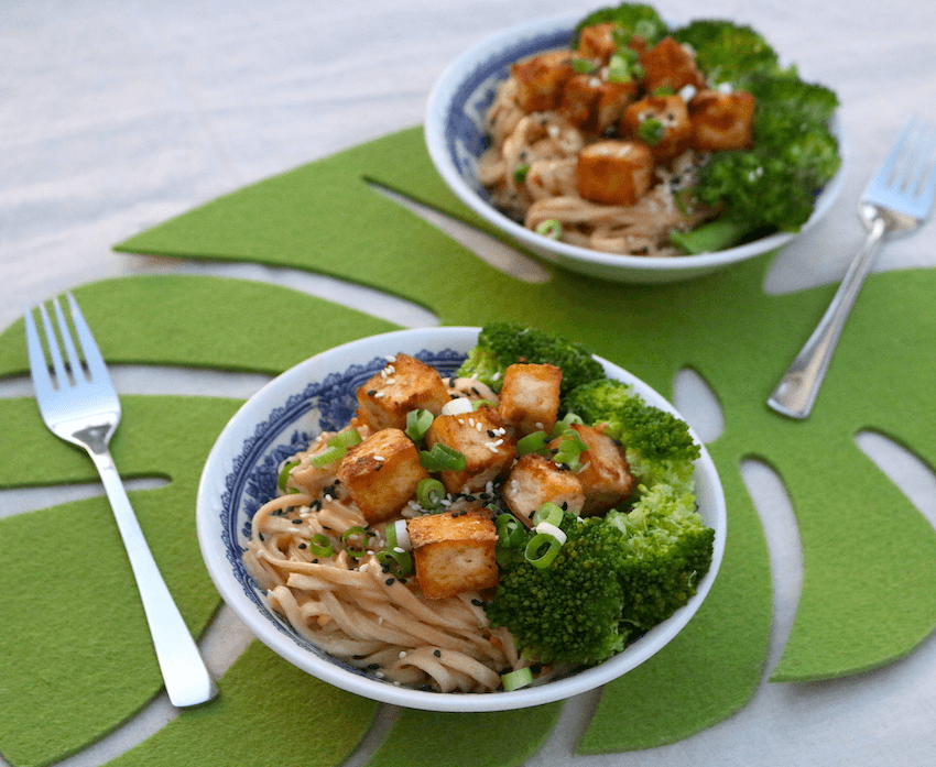 Two bowls of peanut noodles topped with golden tofu and florets of broccoli. 