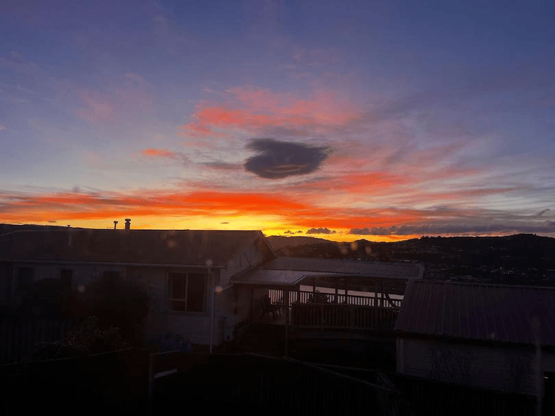 The sun rising above the hills with a with a house in the foreground 