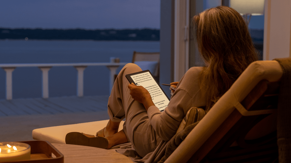 A woman sits with her Kindle reader jotting down notes.