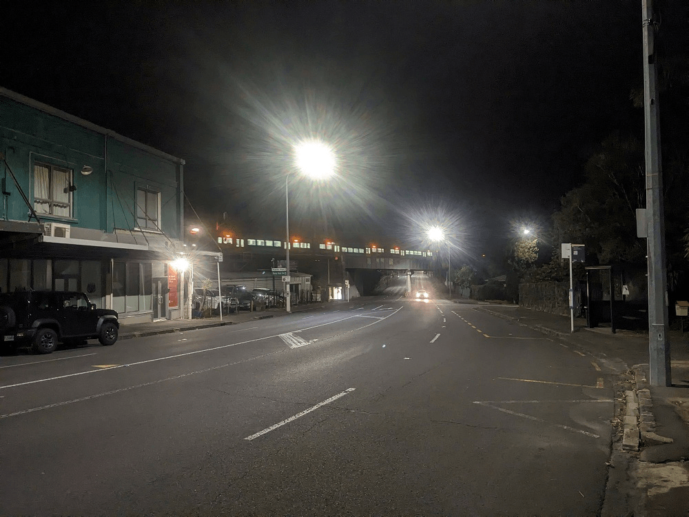 bad photo of a train going over an overpass and bright flare from streetlamps at night